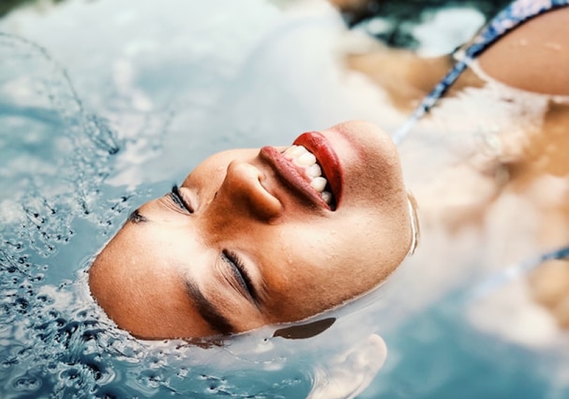 Woman smiling with eyes closed, partially submerged and floating in clear water.