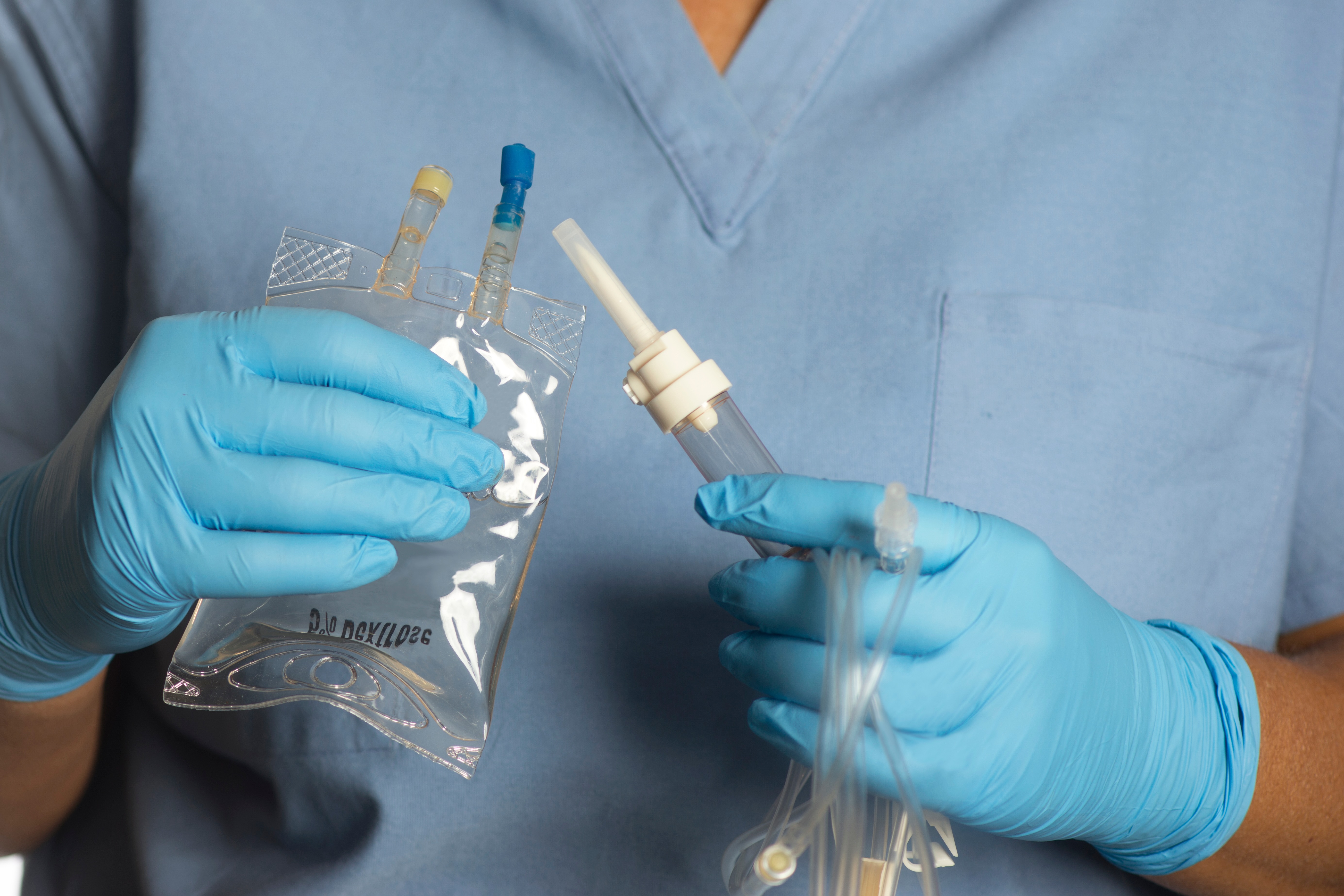 Person wearing blue gloves and scrubs holding a medical infusion bag and tubing.