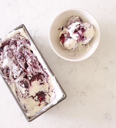 Loaf pan of no-churn vanilla ice cream with blackberry swirls beside a bowl of scoops