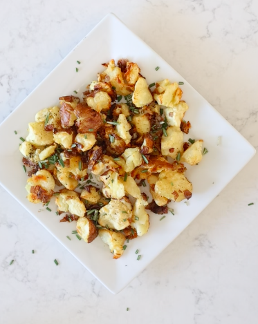 Crispy smashed red potatoes with browned edges, fresh rosemary and chopped herbs on a square white plate.