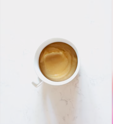 White mug of smooth homemade applesauce on a white marble counter, seen from above.