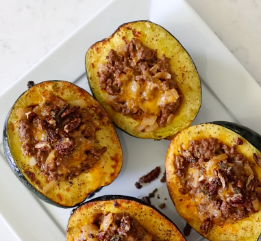 Roasted acorn squash halves on a white platter, stuffed with ground beef and melted cheddar and topped with toasted pecans and a drizzle of hot honey.