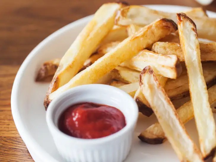 Plate of golden oven-baked homemade fries with a small cup of ketchup.