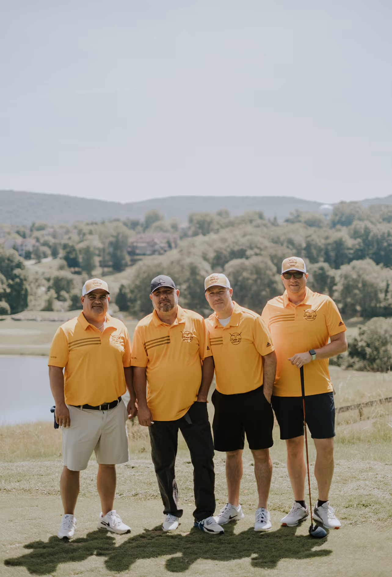 Four men in yellow shirts smile for a photo on a sunny golf course.