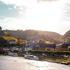 River with several docked boats and a hillside town under a bright sky.