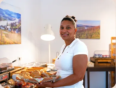 Smiling woman in a white shirt holding a basket of assorted bread in a bright kitchen setting.
