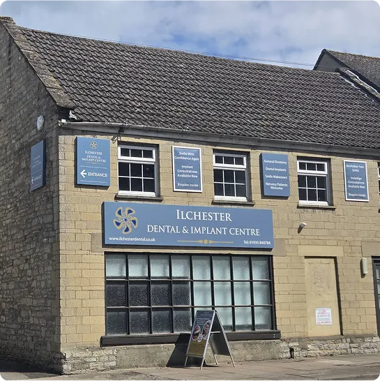Stone building with multiple blue signs for Ilchester Dental & Implant Centre including services and contact details.