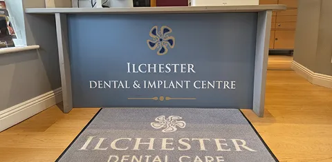 Reception desk with Ilchester Dental & Implant Centre logo and matching floor mat in a dental clinic.