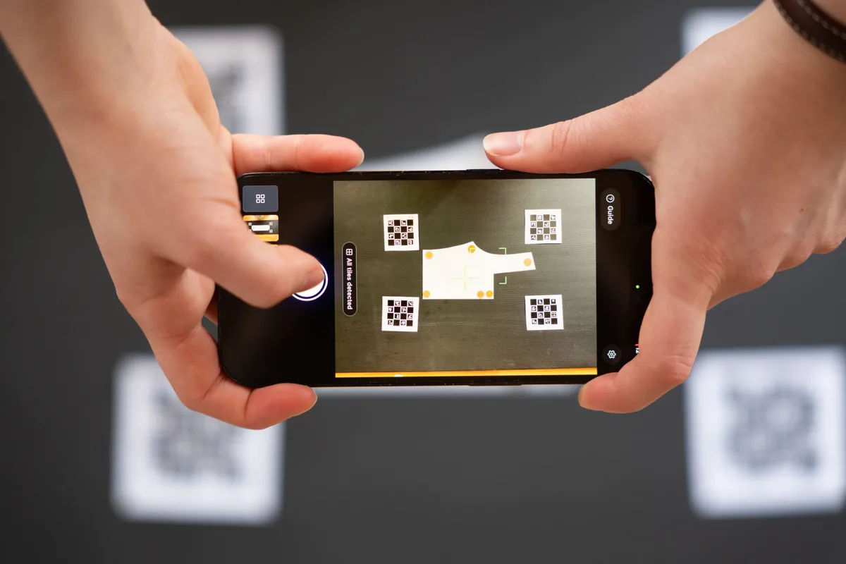 Phone held over a pattern piece with four Reference Tiles, the app shows All tiles detected