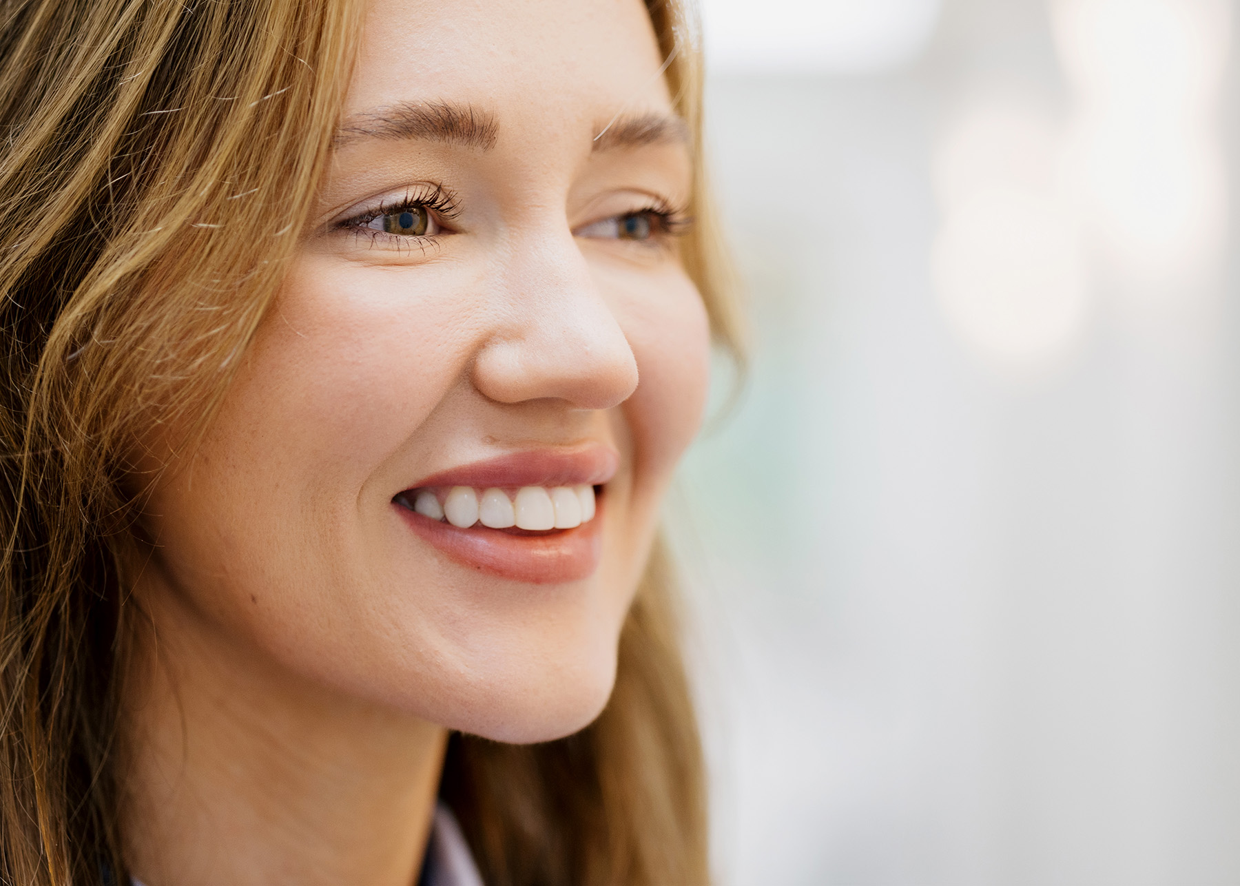 Close-up of a smiling woman with light brown hair looking to the side.