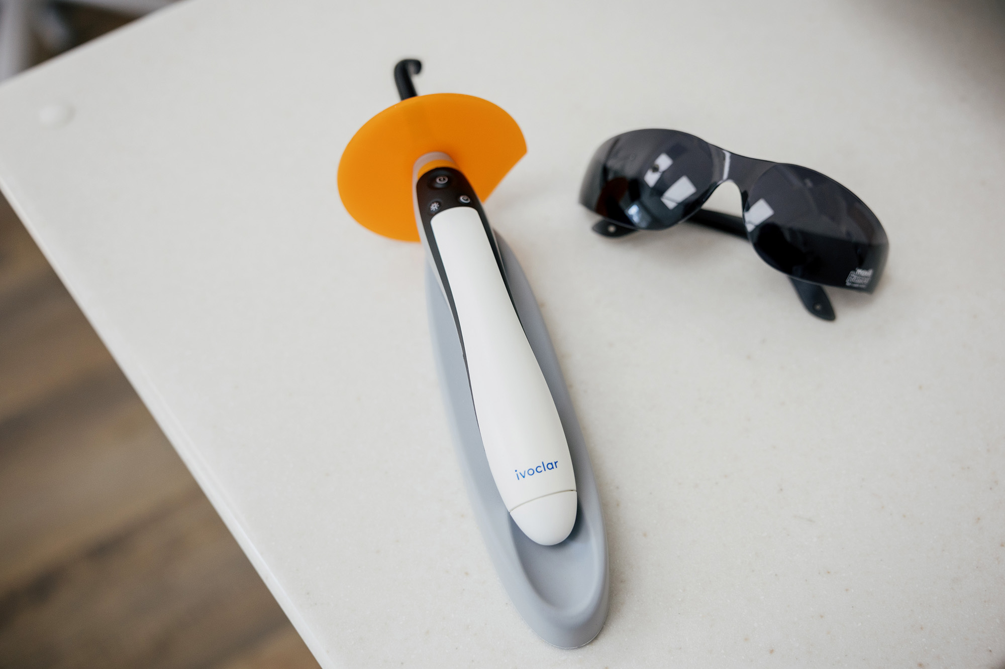 Ivoclar dental curing light device with orange shield and protective black sunglasses on a white surface.