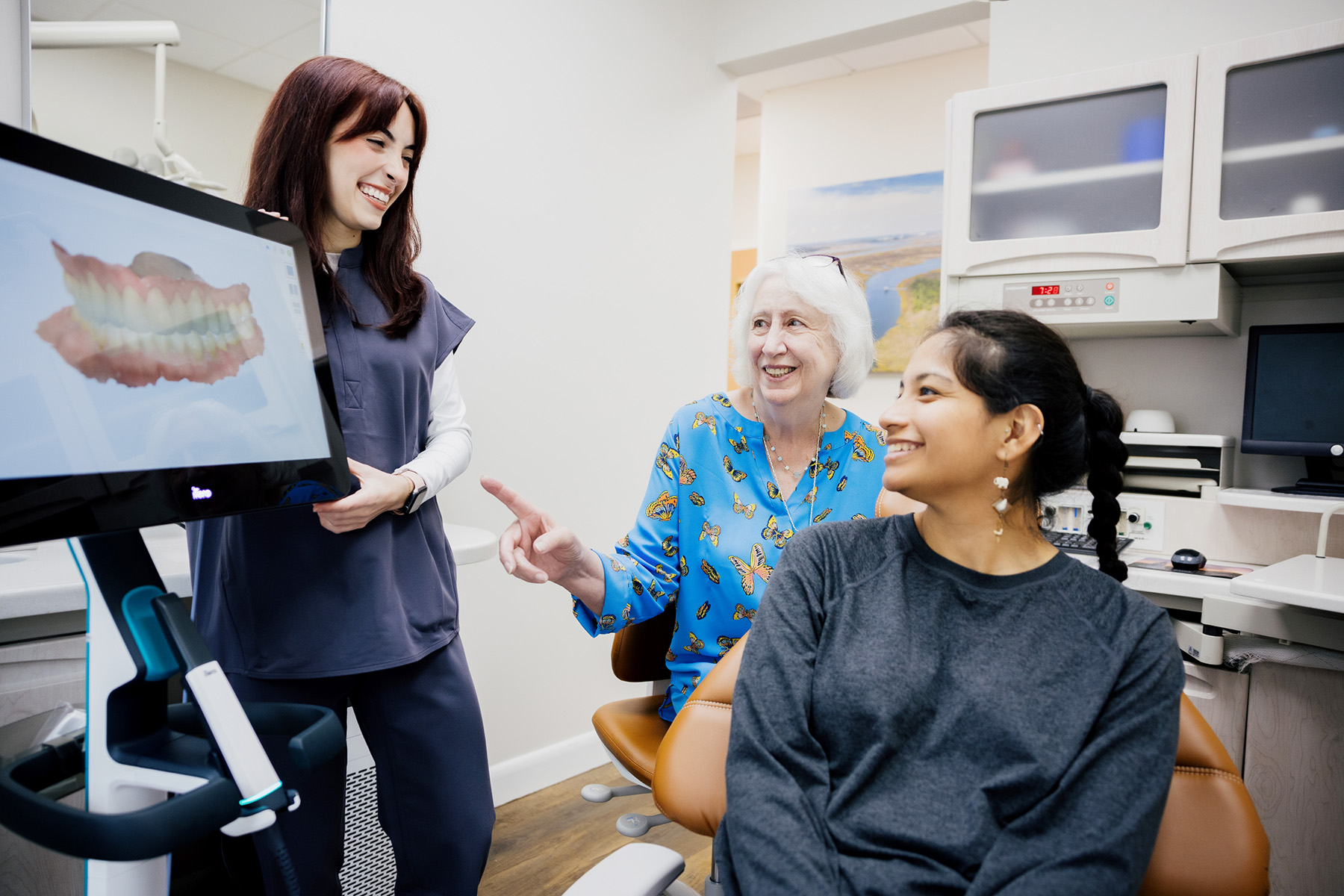 Dentist explaining a digital dental scan to a smiling elderly woman and a younger woman in a dental office.