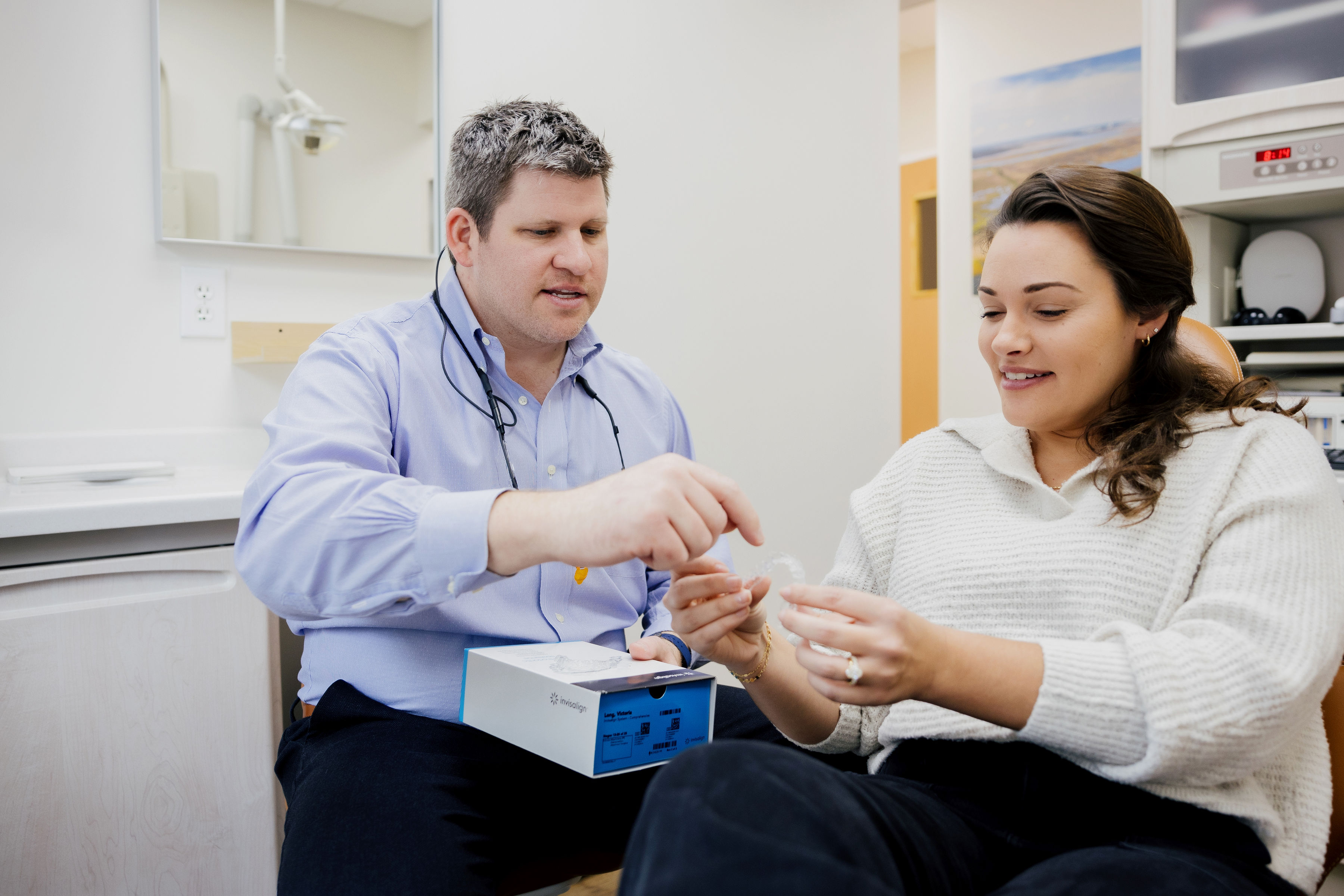 Dentist explaining Invisalign clear aligners to a smiling female patient in a dental office.