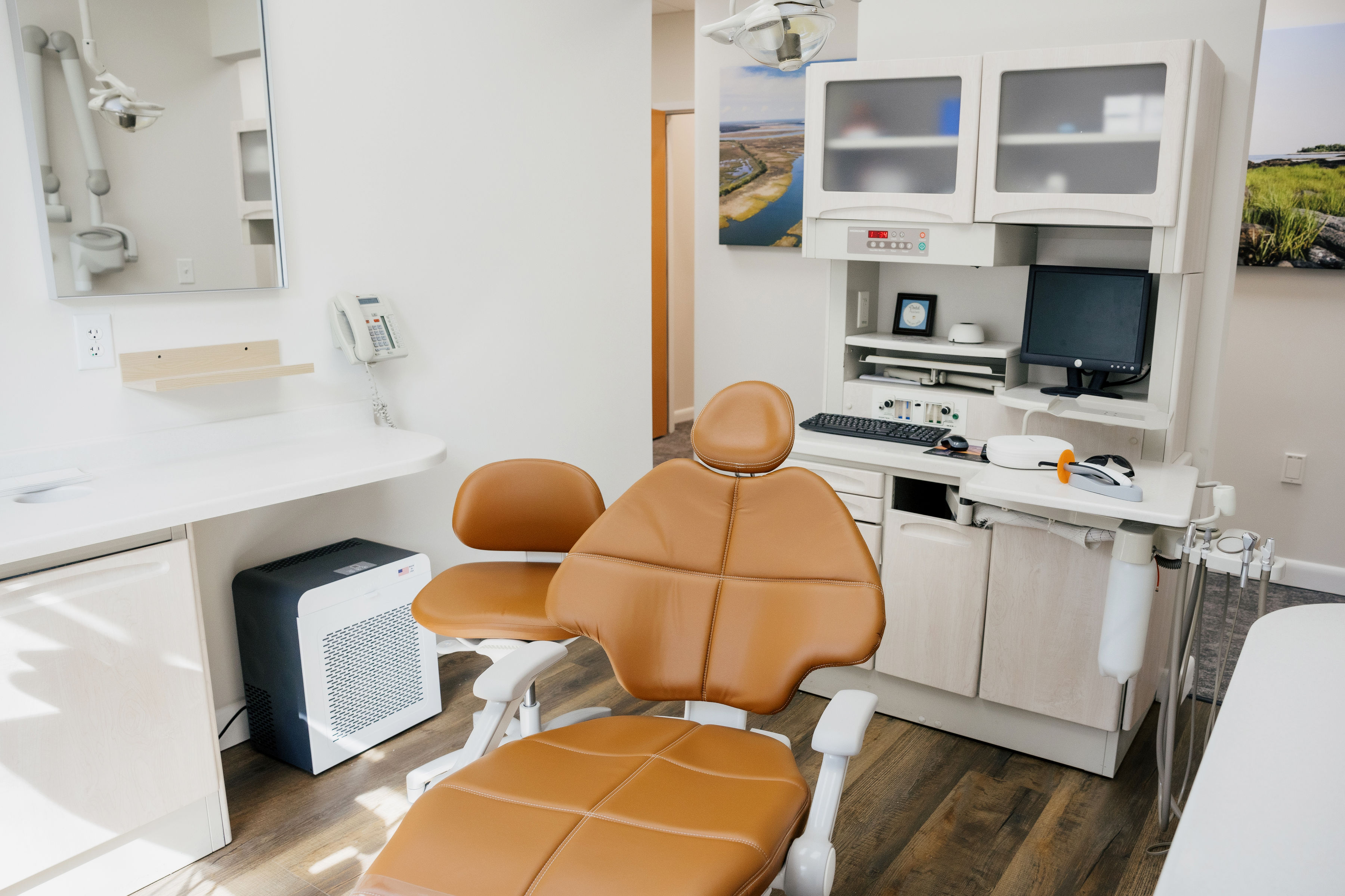 Modern dental examination room with tan dental chair, computer workstation, and dental instruments.