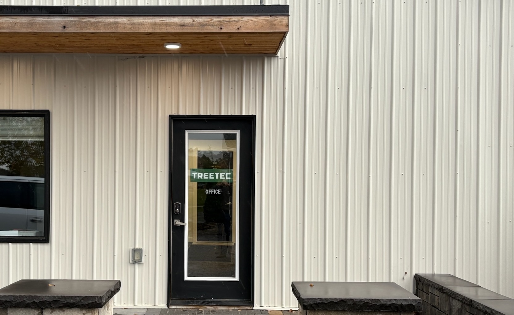 Black-framed glass door with the text 'Employees Treetec Office' on a beige corrugated metal building exterior.