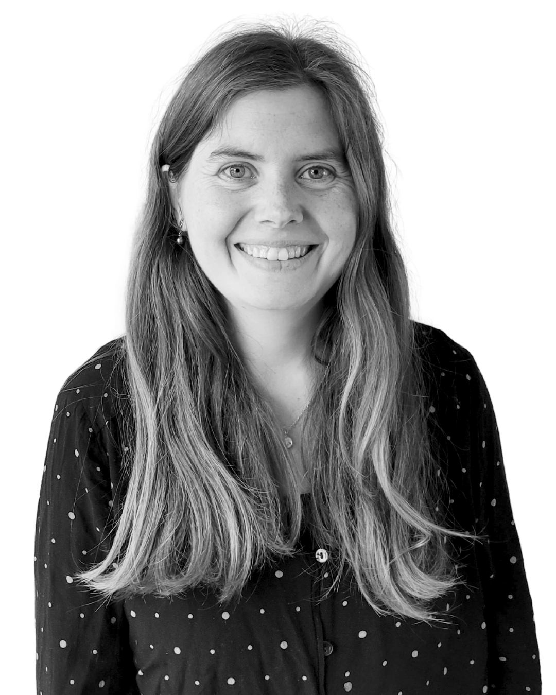 Smiling woman with long hair wearing a dark, polka-dot blouse against a plain background.