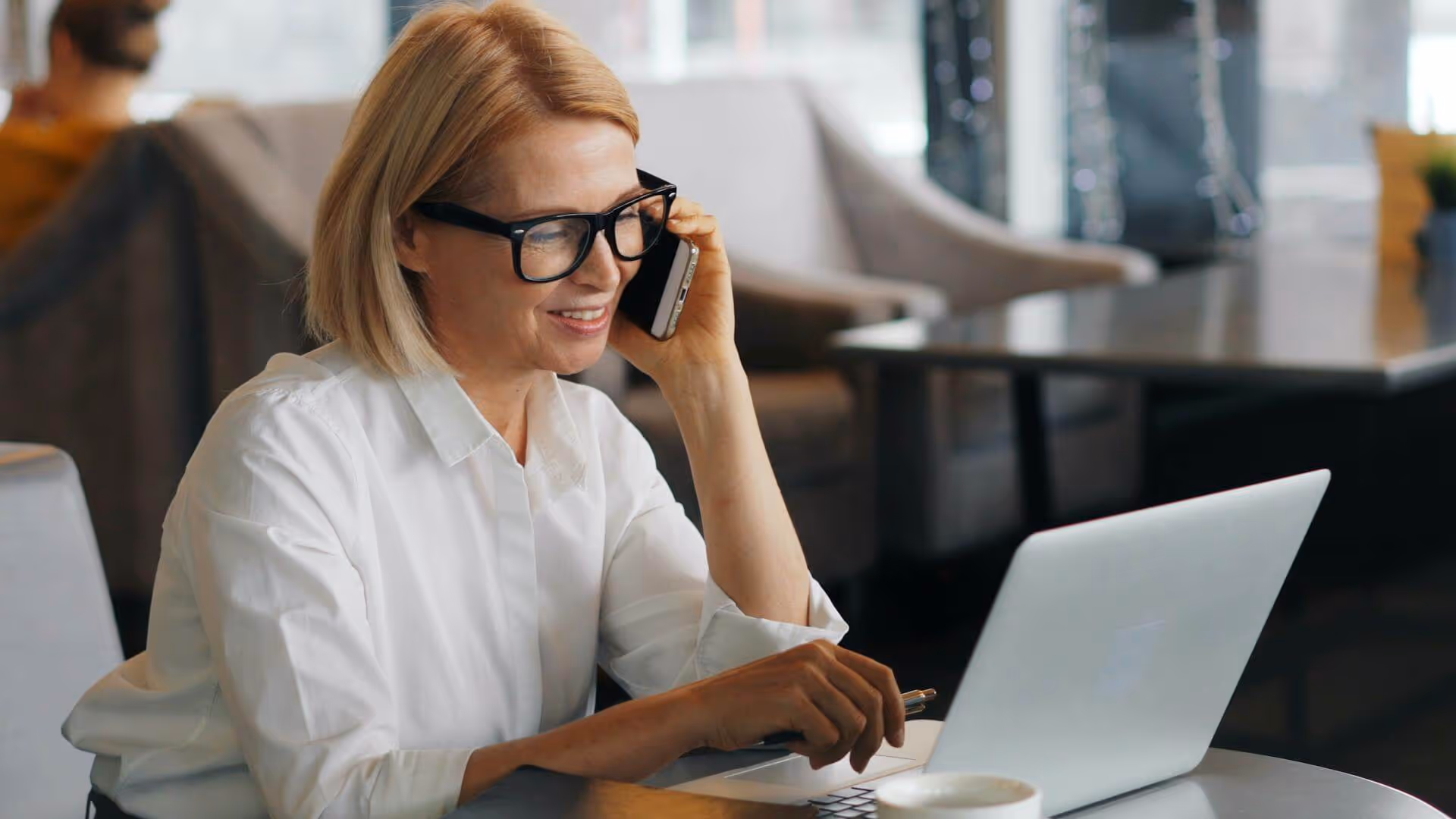 A woman wearing glasses and a white shirt is using a laptop.