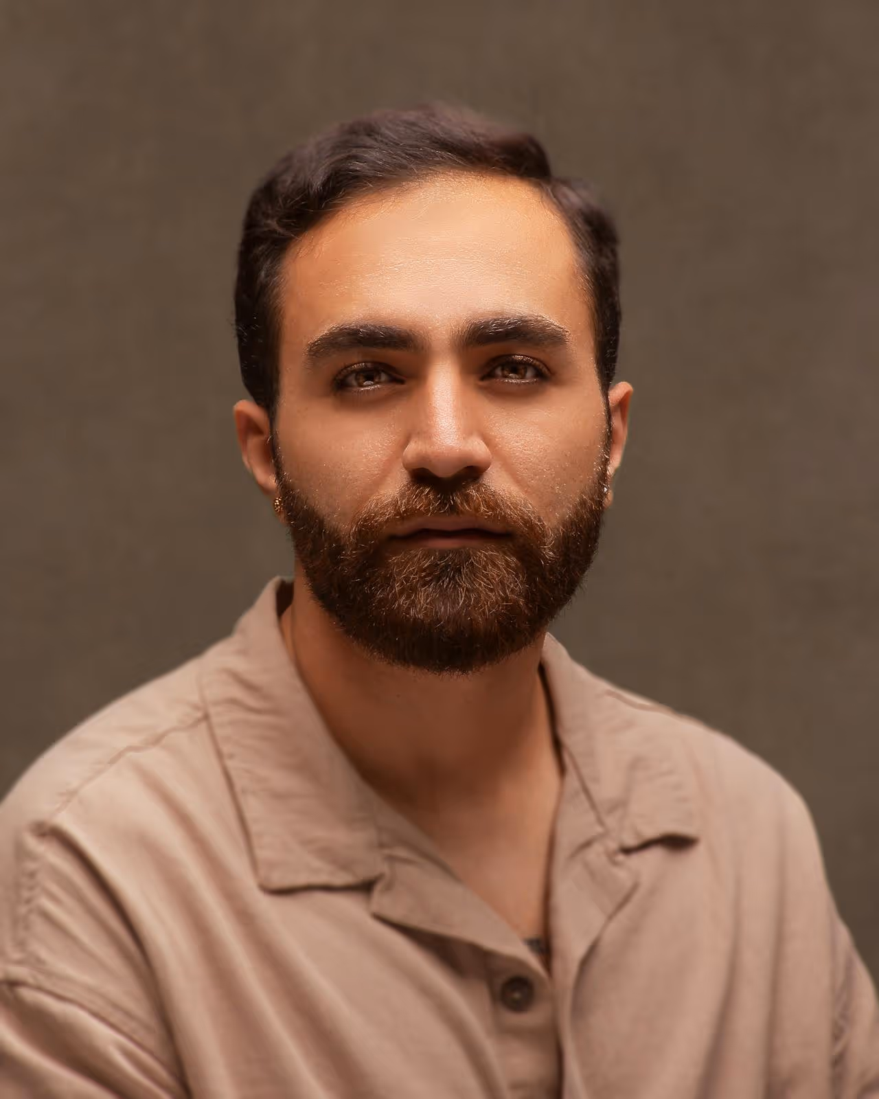 Portrait of a man with a beard wearing a beige button-up shirt against a plain background.