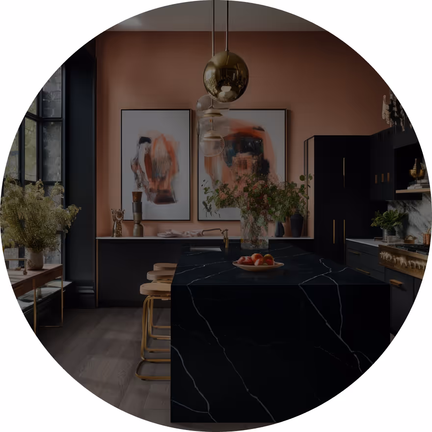 A modern kitchen featuring a black marble island and cabinetry. Walls are painted in a soft peach color, and there are framed abstract artworks. The space includes decorative plants and stools for seating.