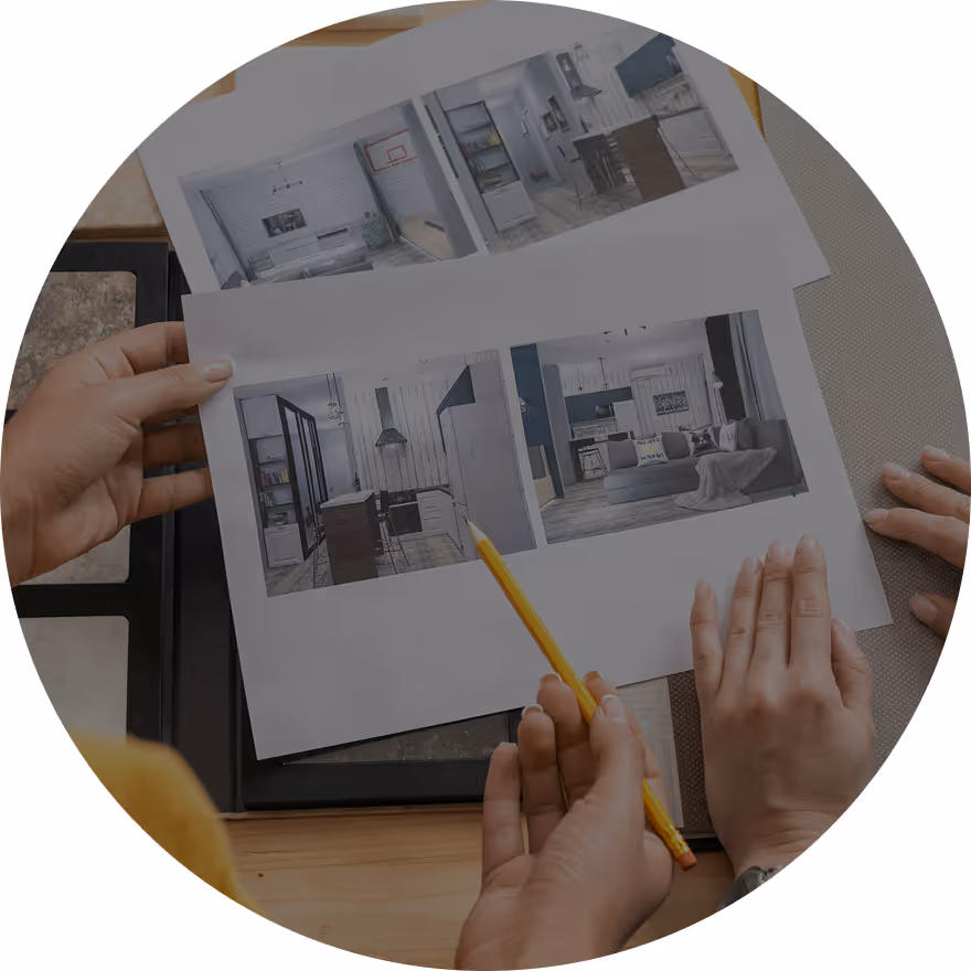 Two individuals discussing design plans with printed images of interiors placed on a table. One person is holding a pencil, pointing at the images.