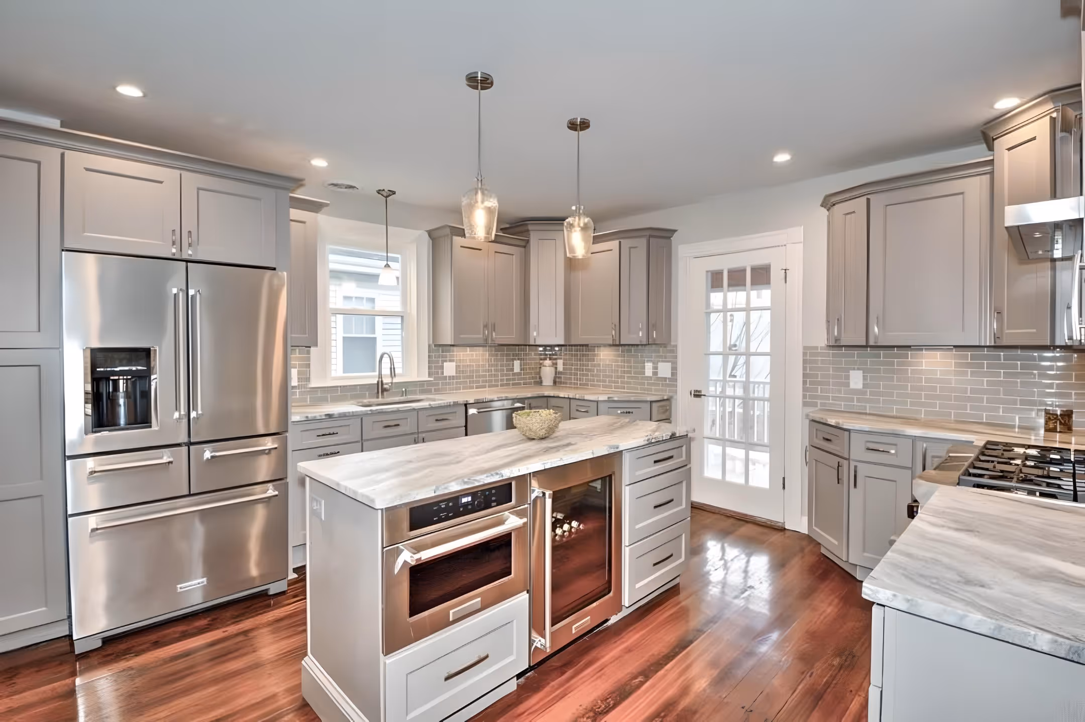 A kitchen with a stainless steel refrigerator and grey cabinets.