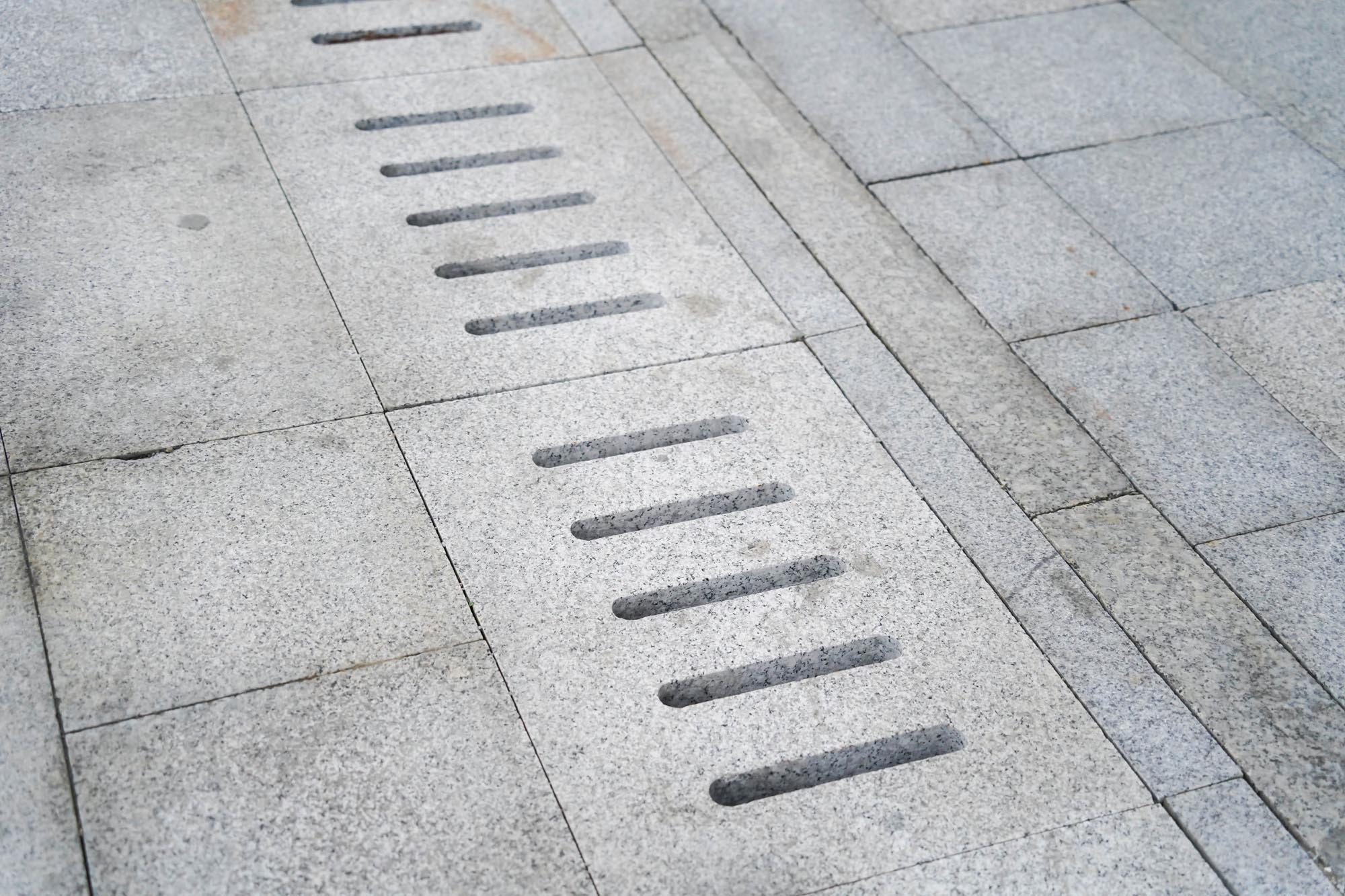 A sidewalk drain with multiple holes, located in Avalawn, allowing water to flow through.