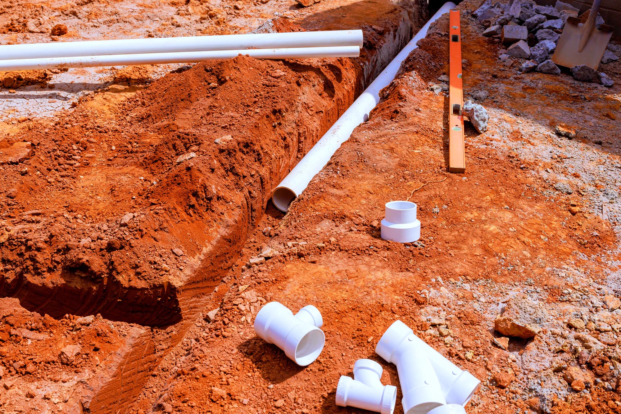A pipe resting on the ground next to another pipe and multiple white pipes, showcasing Grading and Re-sloping