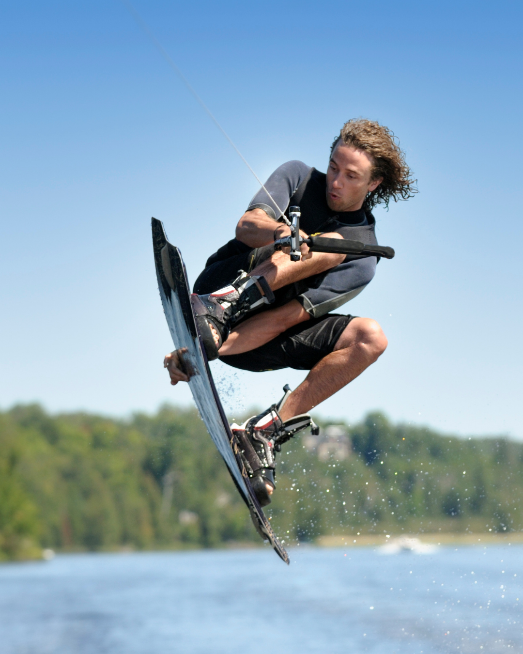 A wakeboarder, mid air, hitting a frontside heel grab.