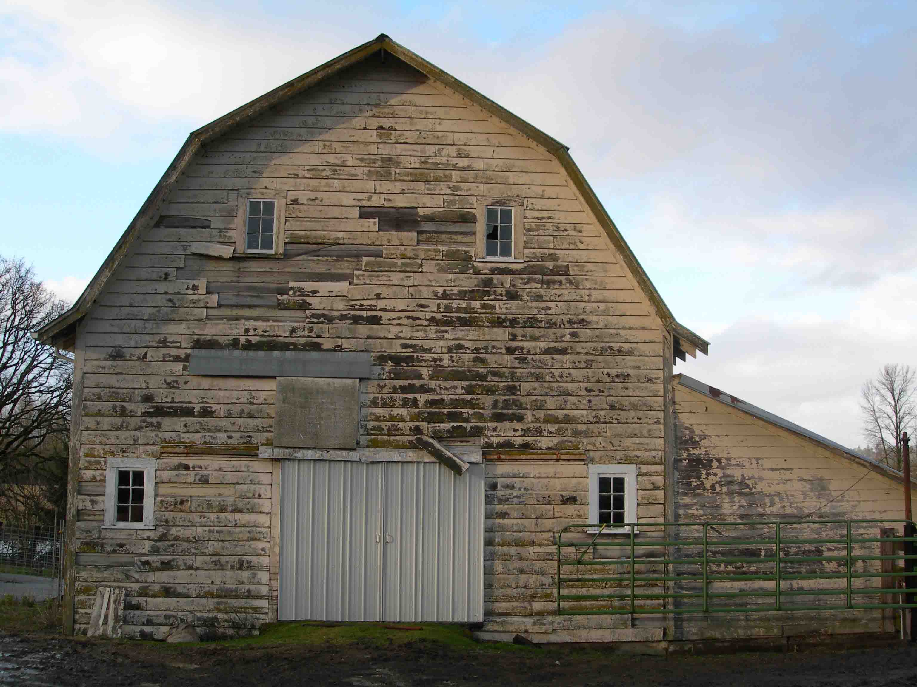 Outdoor event setup with round tables covered in pastel-colored tablecloths, wooden chairs, glassware, floral centerpieces, and string lights overhead.