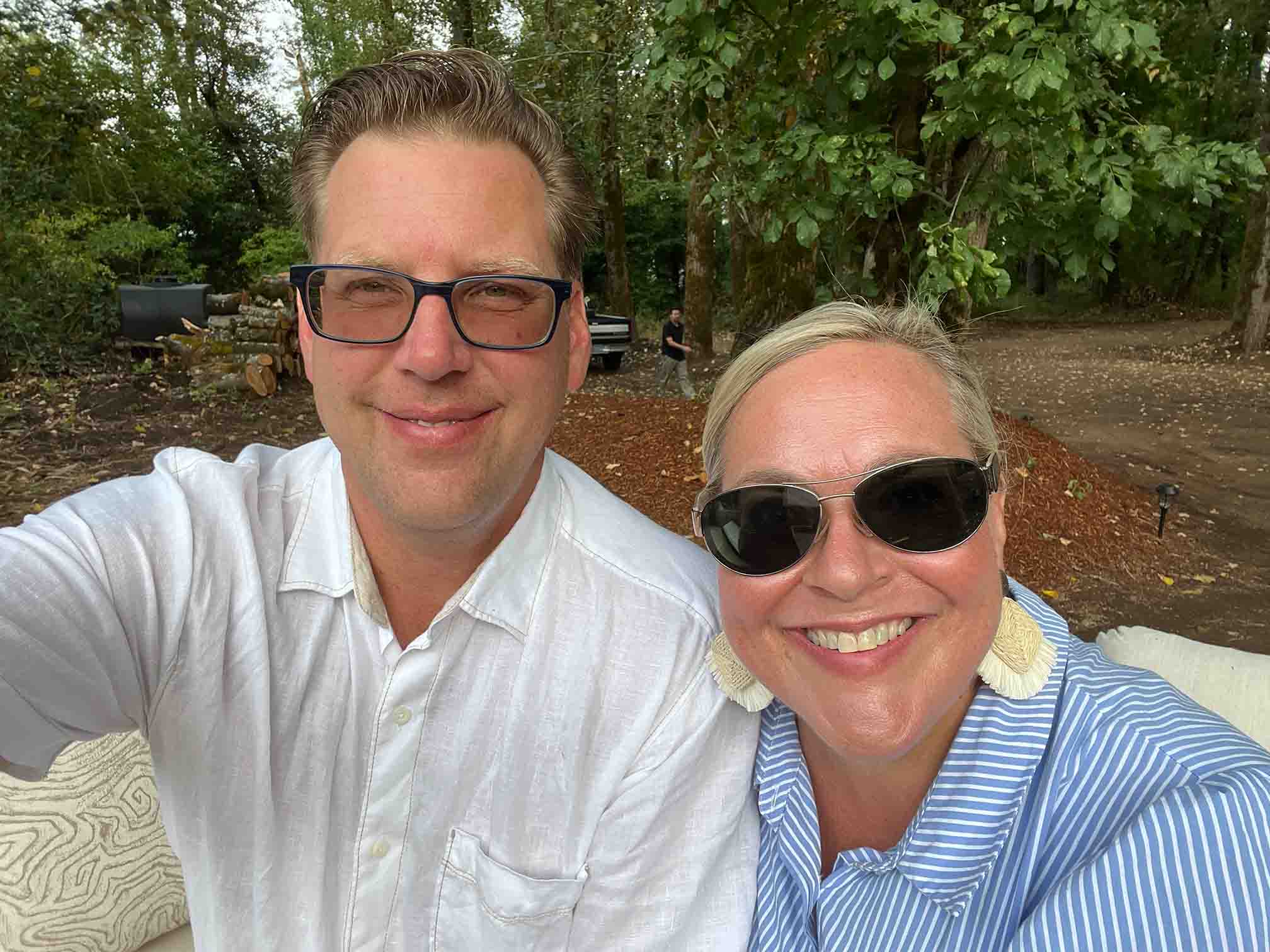 Couple in wedding attire holding hands and gazing at each other in a sunlit forest setting during sunset.
