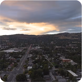 Aerial view of a city street running toward a mountain range at sunset with clouds in the sky.