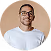 Smiling man with glasses and a white shirt against a peach background.