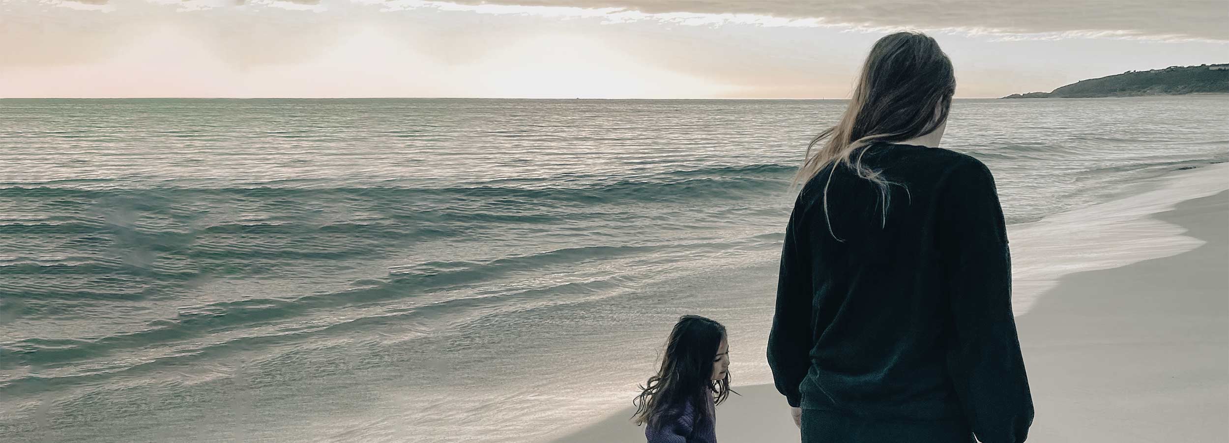 image of lucy blair chung and her daughter walking up a beach from behind