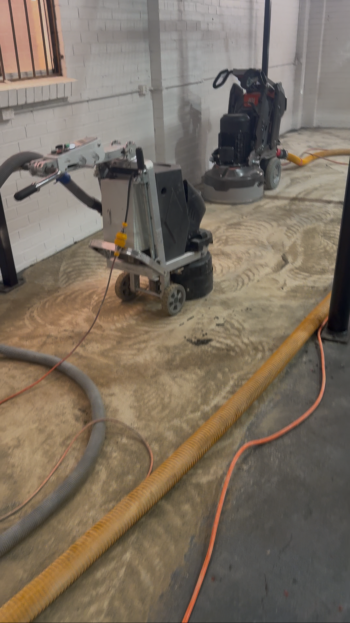 Two floor grinders removing sticky adhesive from a private gym concrete slab