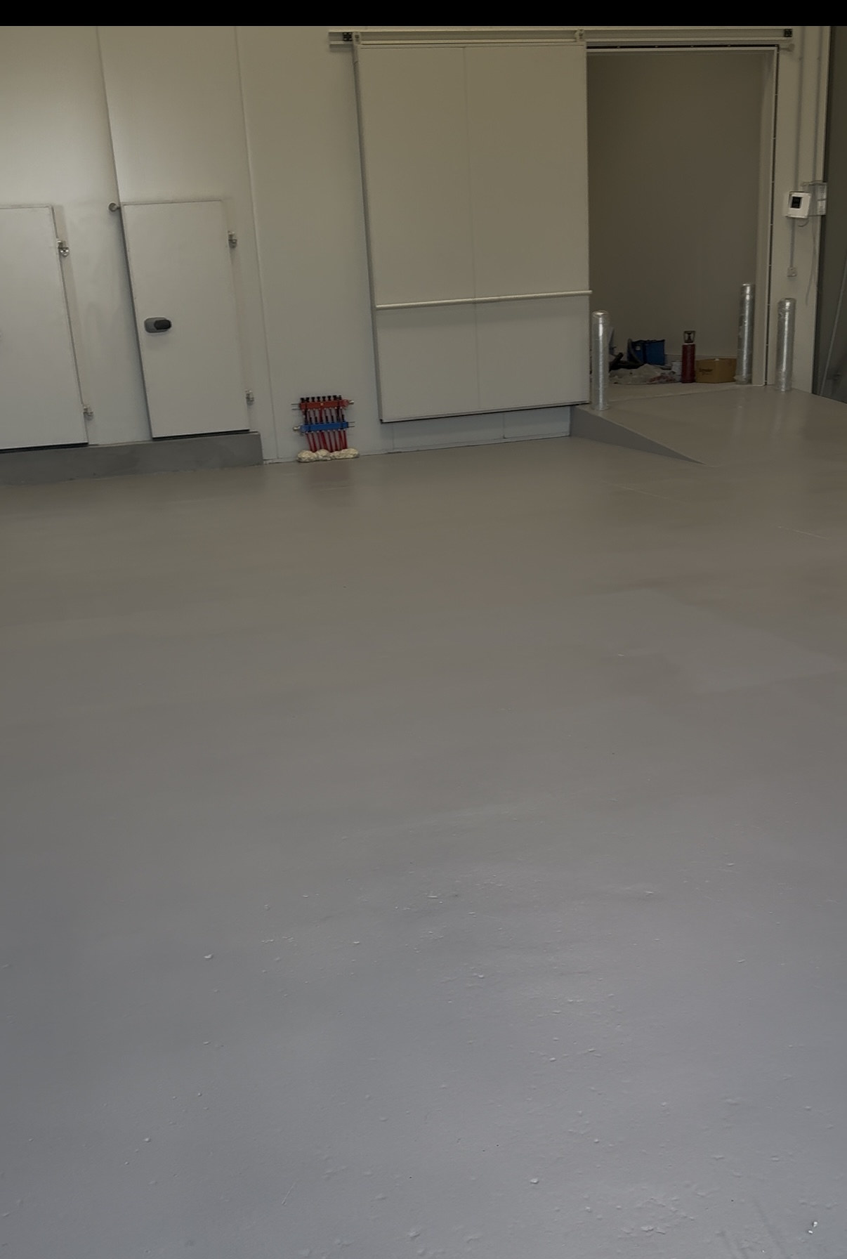 Completed grey quartz-textured epoxy floor surrounding insulated doors in the food warehouse