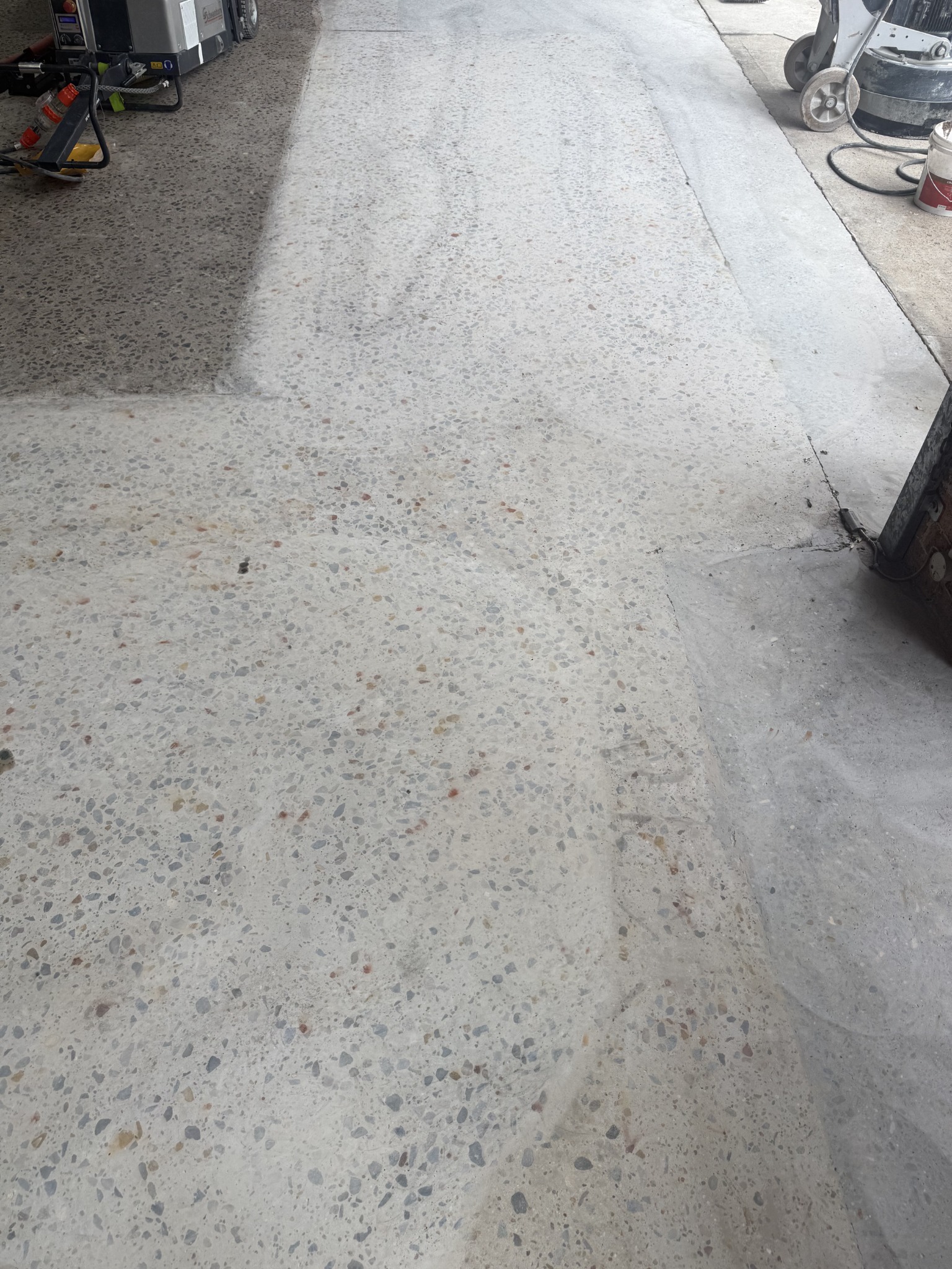 Partially polished concrete developing aggregate exposure beside the grinding equipment