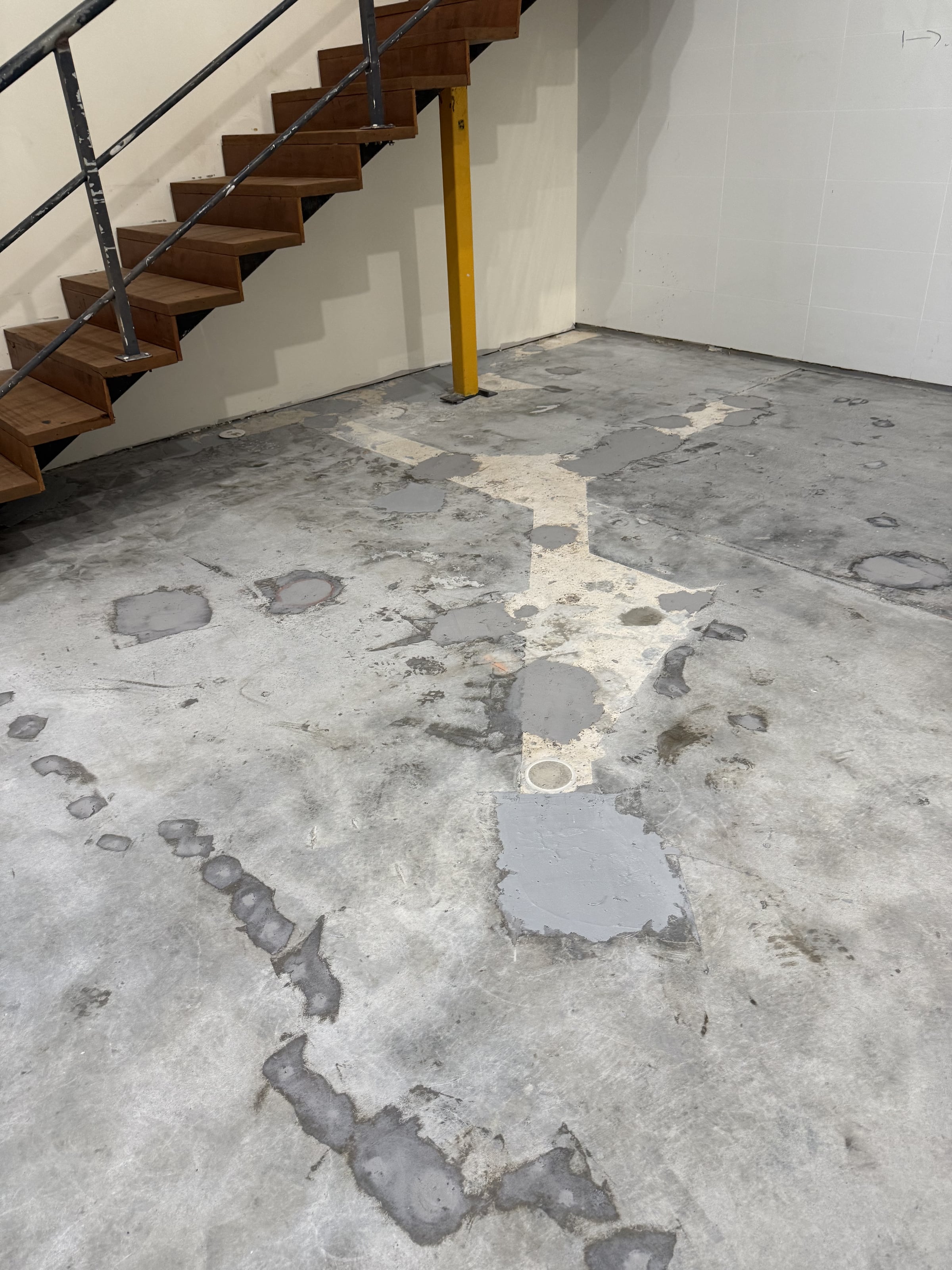 Patched and damaged warehouse concrete beneath stairs before epoxy floor preparation