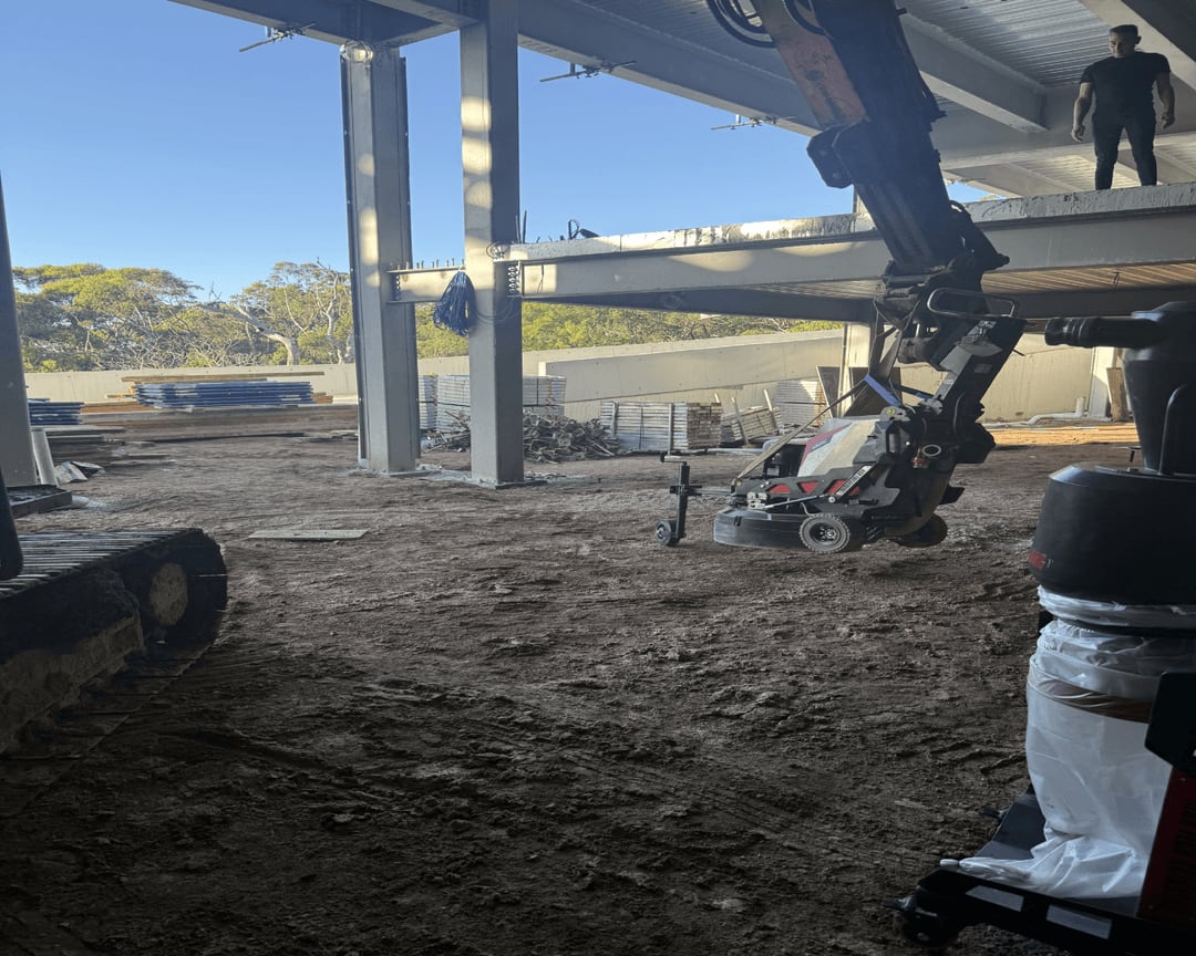 Concrete floor grinder being lifted to an elevated slab with a telehandler