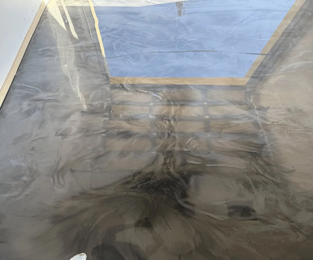 Close view of the glossy gunmetal metallic epoxy floor, showing flowing grey pigment movement and doorway reflections.
