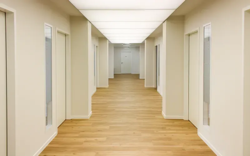 Langer Praxisflur mit Holzfußboden und durchgehender Deckenbeleuchtung.