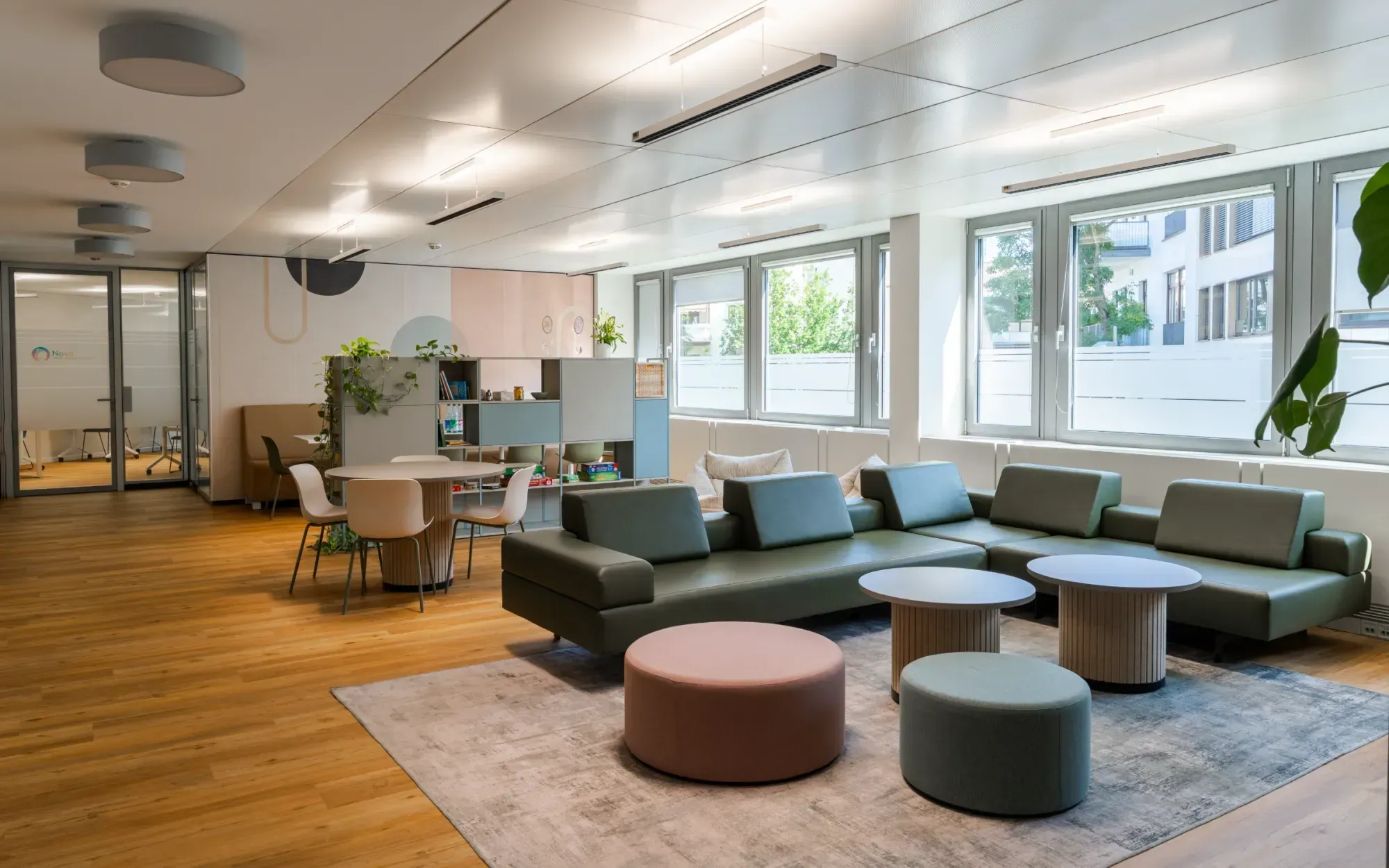 5 Weitwinkelansicht des Aufenthaltsraums mit großem Sofa, Hockern und Fensterfront.