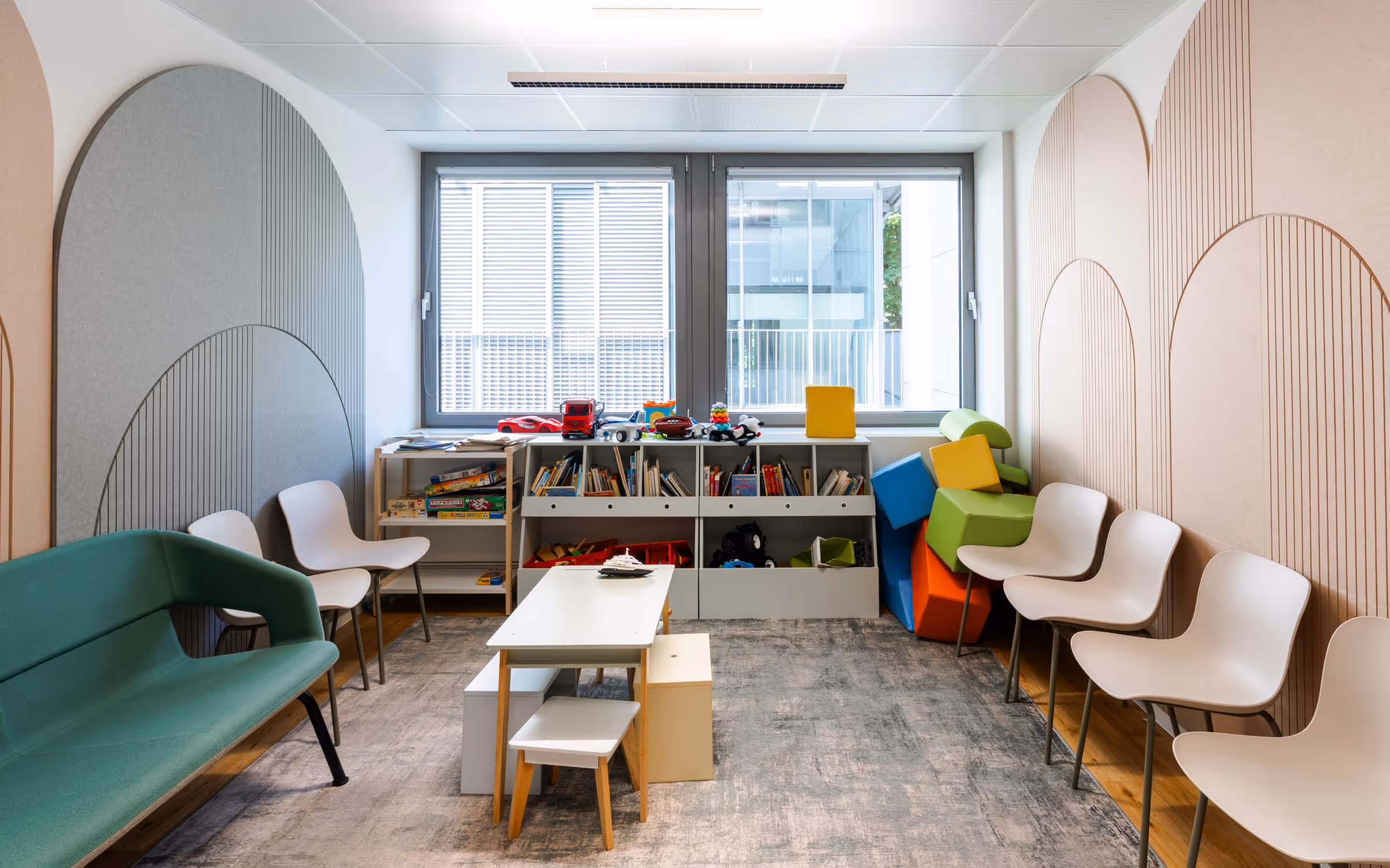 Weitwinkelansicht des Aufenthaltsraums mit großem Sofa, Hockern und Fensterfront.