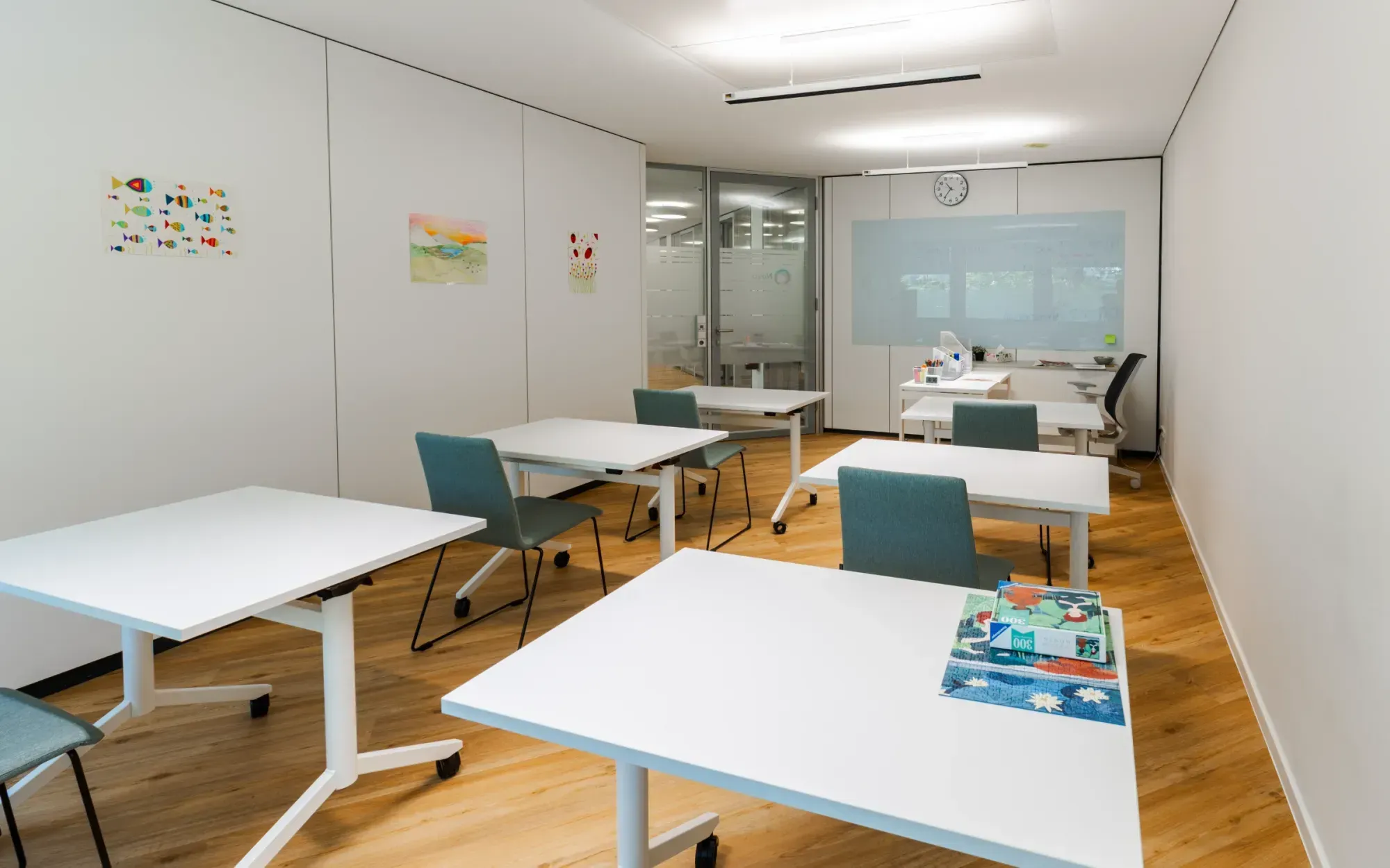 Lern- oder Gruppenraum mit Tischen, Stühlen und einem Whiteboard.