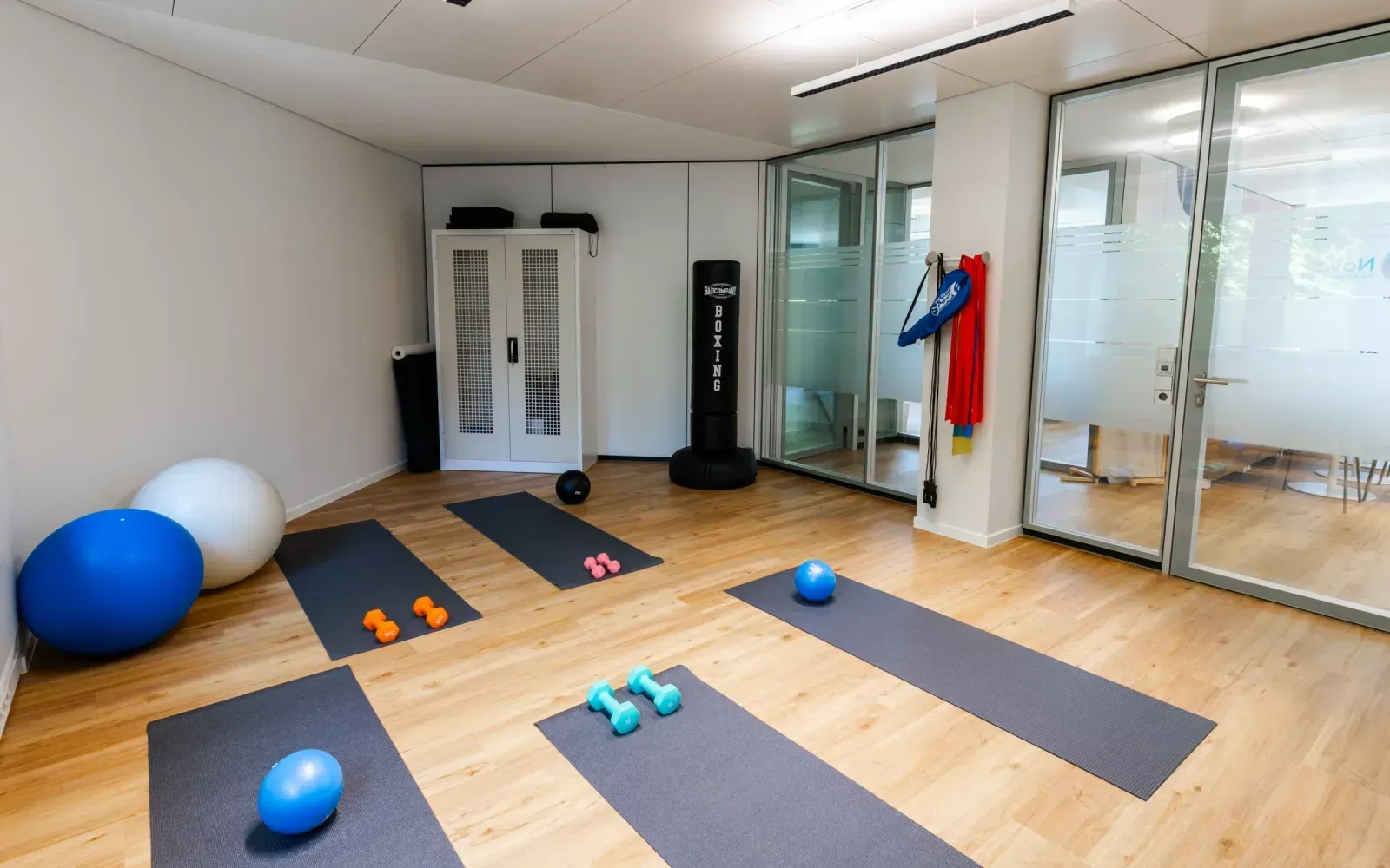Bewegungsraum mit Yogamatten, Hanteln, Bällen und einem Boxsack.