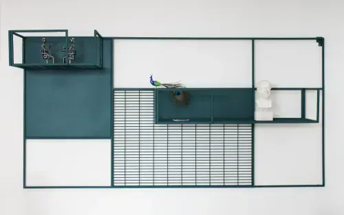 Grünes, geometrisches Wandregal, dekoriert mit Figuren, einer Büste und einer Pfauenfeder.