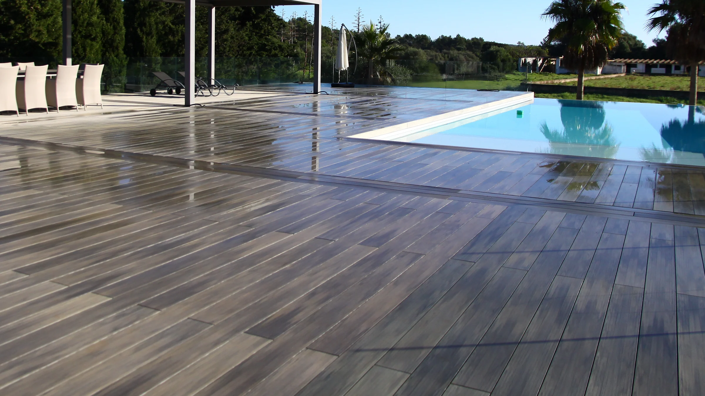 A Tarimatec composite deck laid around an infinity pool on a villa terrace, with a pergola and dining table beyond