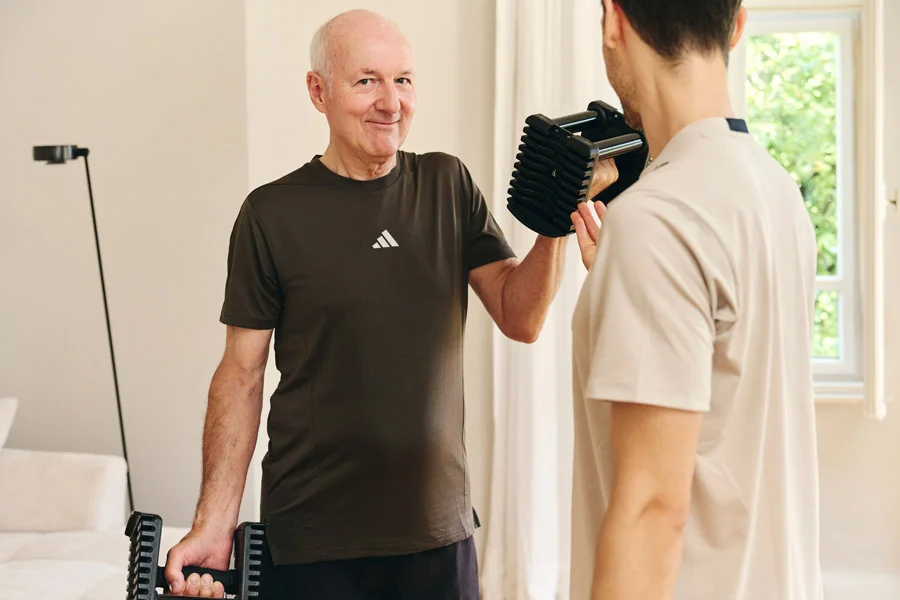 Personal Trainer Lars Traxel korrigiert Hanteltraining eines Klienten im Wohnzimmer.