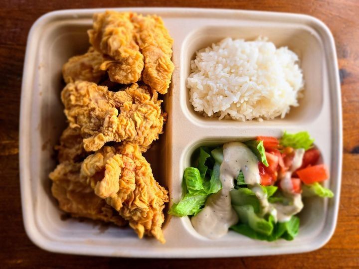 A serving of boneless fried chicken with steamed white rice, side salad, and dipping sauce.