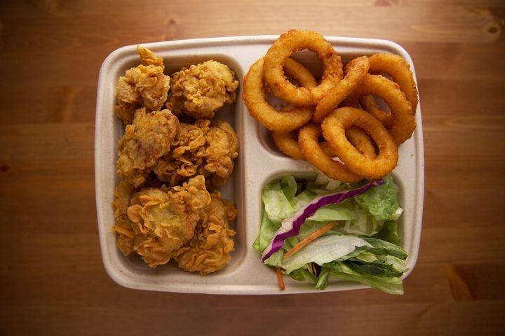 A serving of boneless fried chicken with beer-battered onion rings, side salad, and dipping sauce.