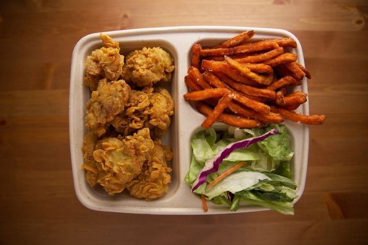 A serving of boneless fried chicken with sweet potato fries, side salad, and dipping sauce.